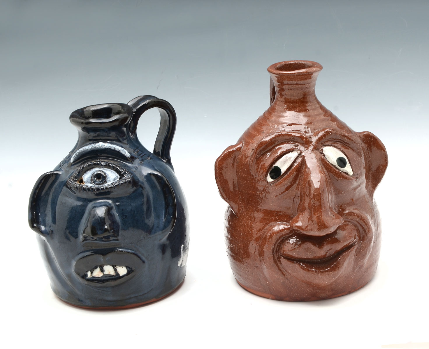 Appraisal: NORTH CAROLINA FACE JUGS Comprising blue glazed Cyclops face handled