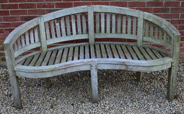 Appraisal: A WEATHERED TEAK GARDEN BENCH with a curved back and