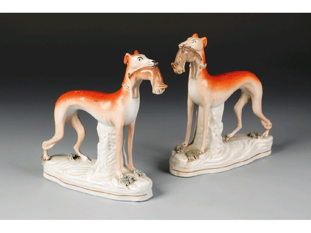 Appraisal: A PAIR OF STAFFORDSHIRE POTTERY GREYHOUNDS modelled standing holding rabbits