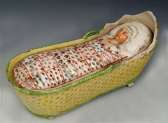 Appraisal: A STAFFORDSHIRE POLYCHROME POTTERY MODEL of a baby in a