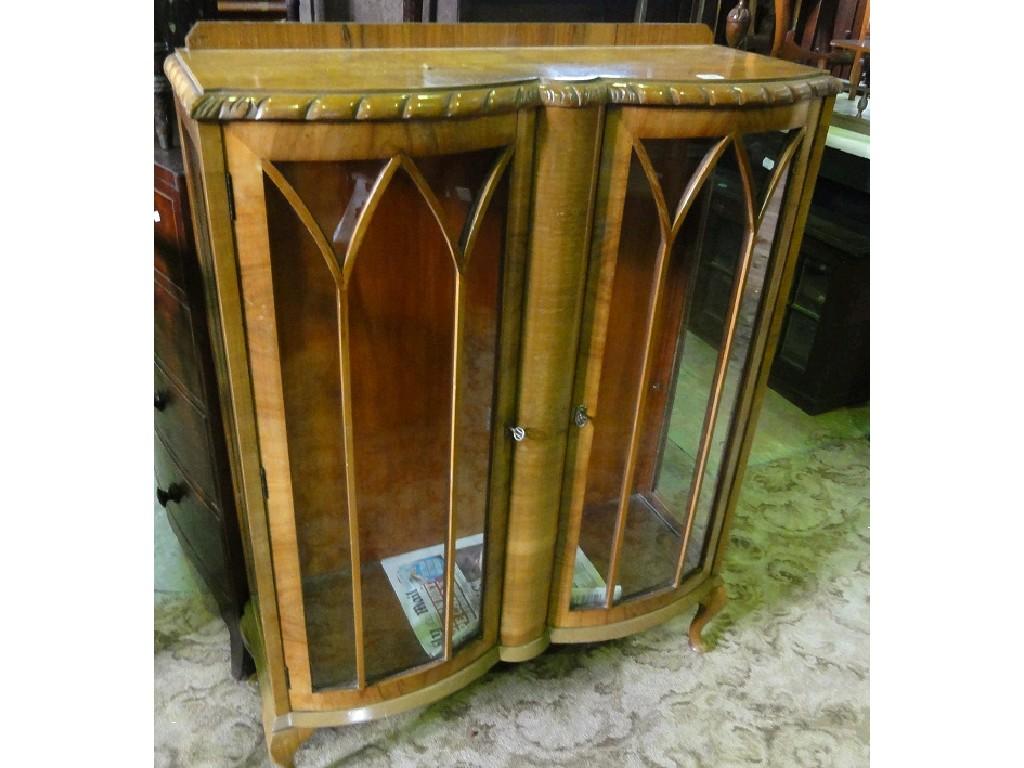 Appraisal: A walnut veneered china display cabinet with serpentine outline enclosed