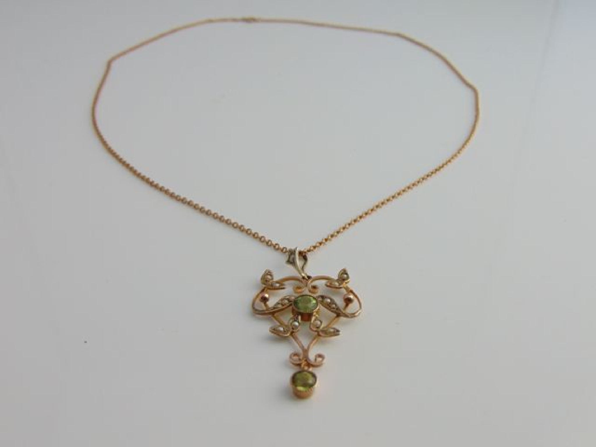 Appraisal: An Edwardian seed pearl and peridot pendant of scrolling open-worked