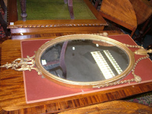 Appraisal: A giltwood oval mirror with urn pediment and trailing festoons