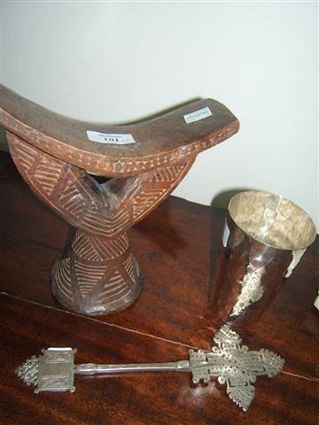 Appraisal: A carve wooden African headrest a beaten metal beaker and