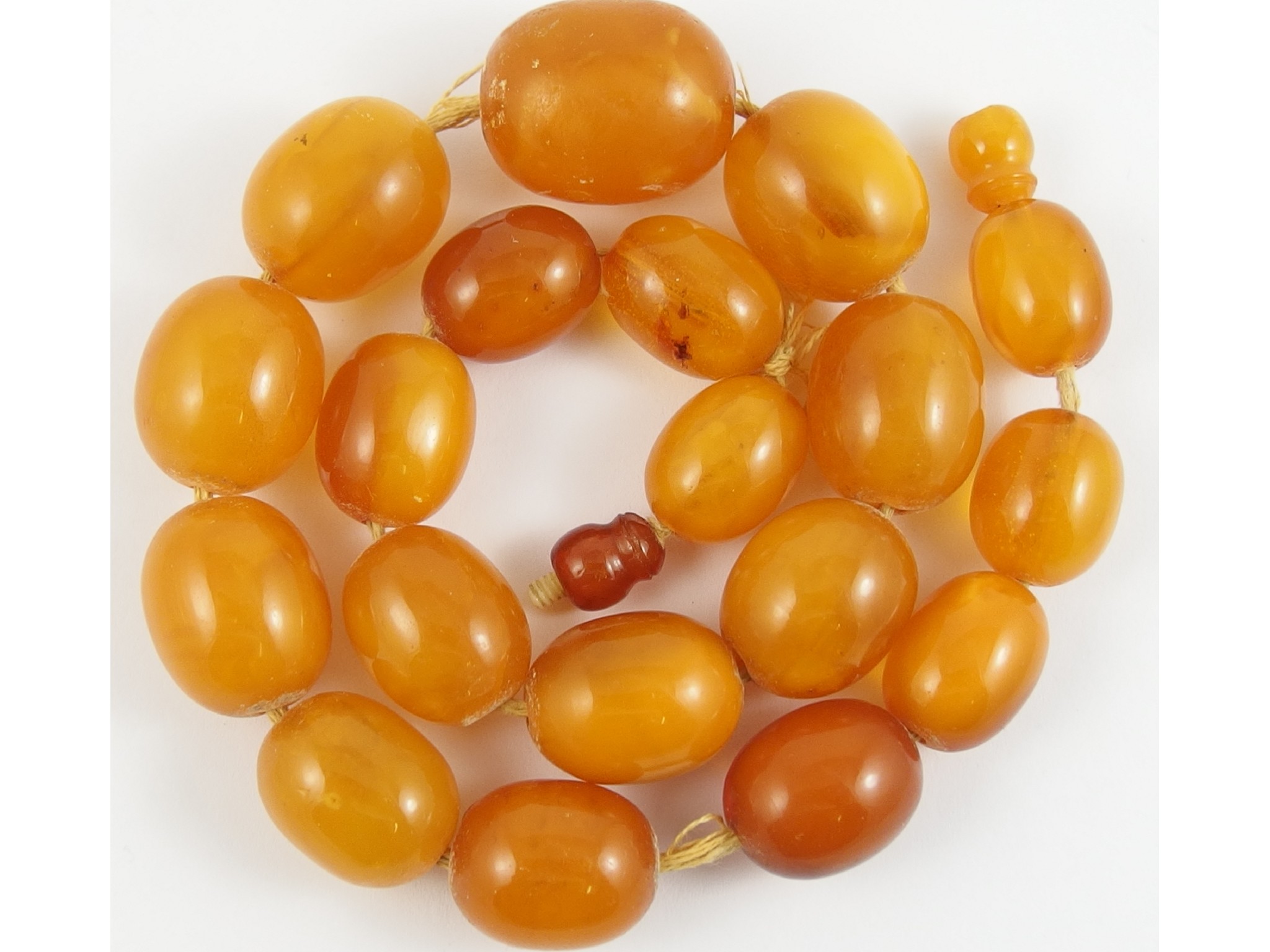 Appraisal: A string of amber coloured beadsin yellow and orange opaque