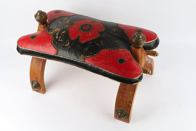 Appraisal: A RED AND BLACK LEATHER UPHOLSTERED CAMEL SADDLE on shaped