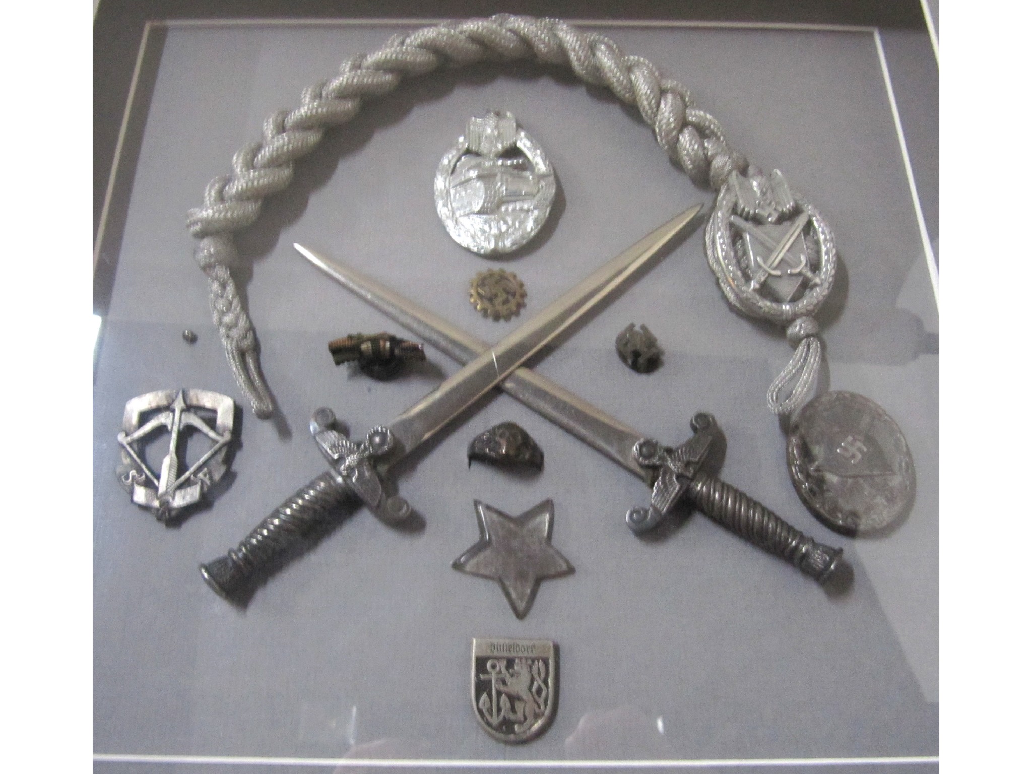 Appraisal: A mounted and framed display of reproduction German daggers badges