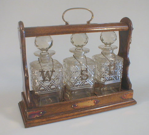 Appraisal: An Edwardian oak three bottle Tantalus with plated mounts and