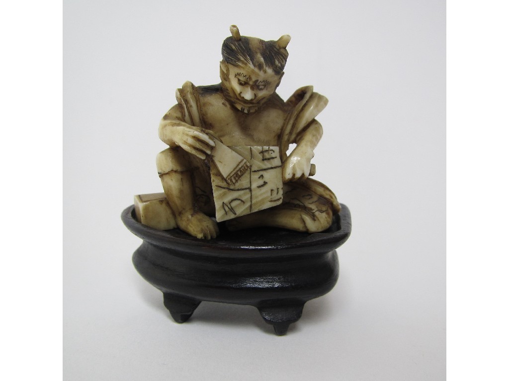 Appraisal: A Japanese carved ivory oni seated holding a fan and