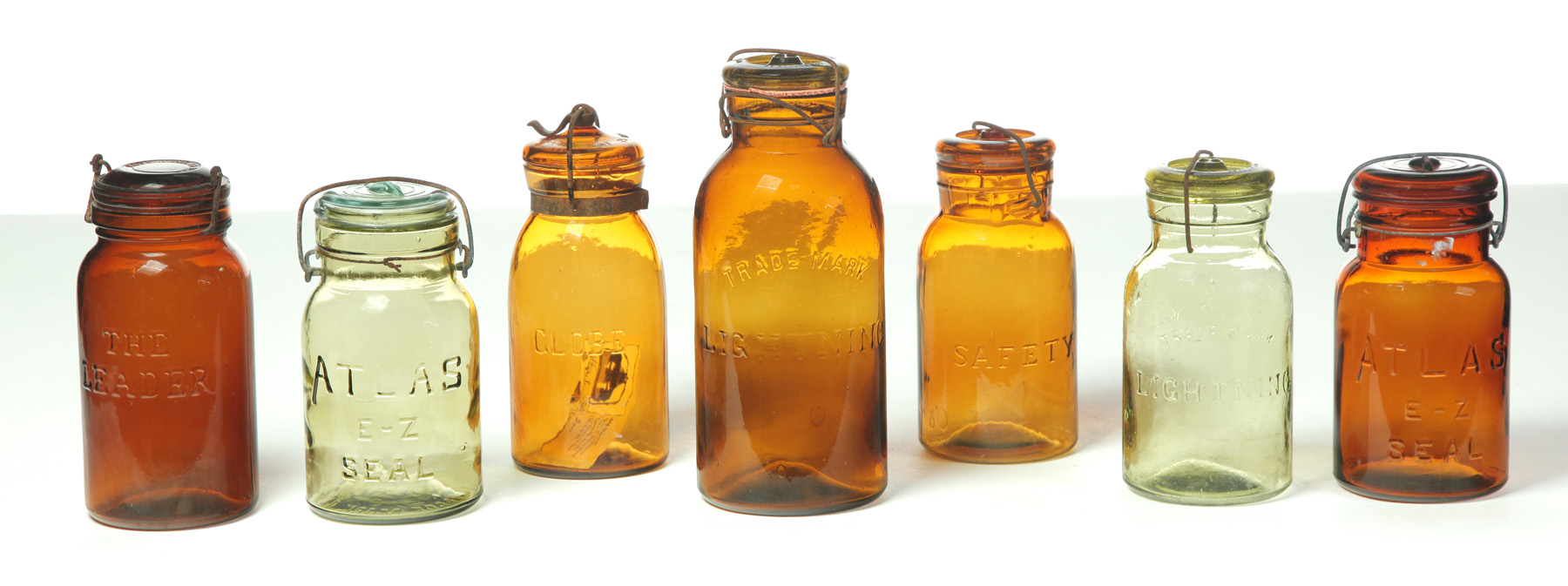 Appraisal: SEVEN CANNING JARS WITH SNAP-CAGE LIDS IN AMBER AND GREEN