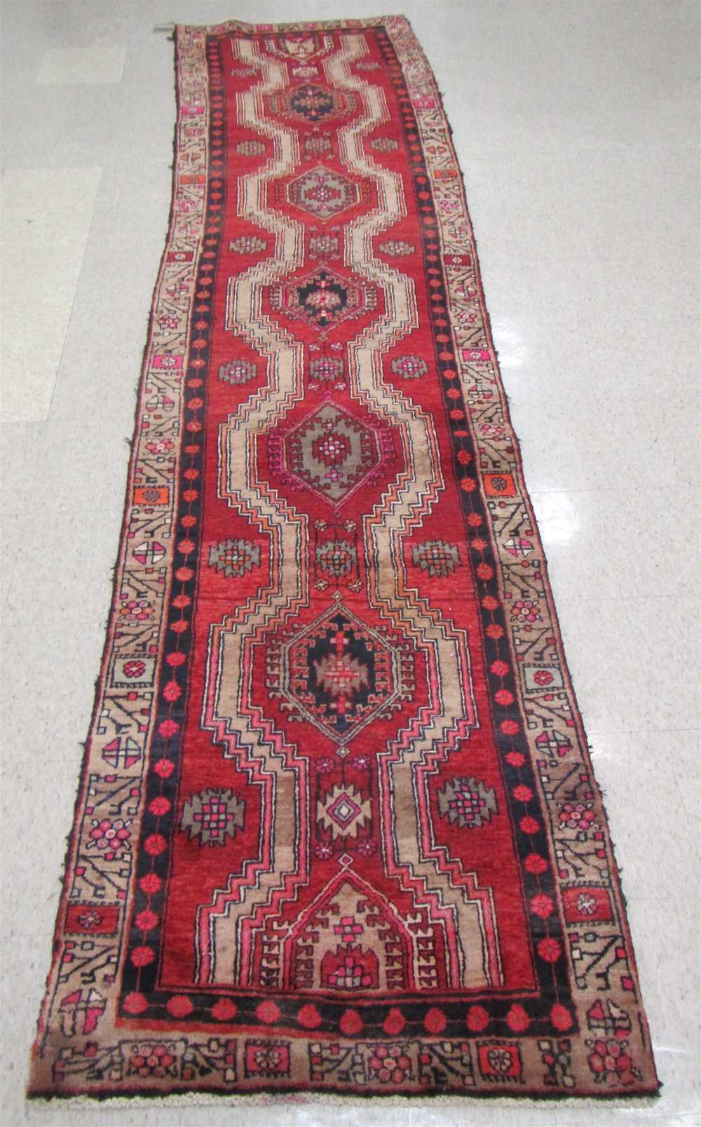 Appraisal: PERSIAN TRIBAL RUNNER repeating geometric medallion design on red ground