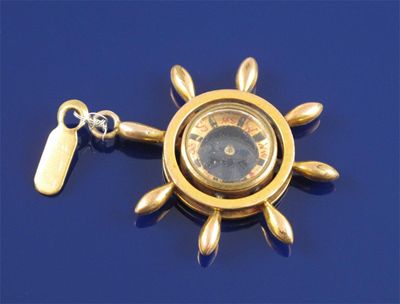 Appraisal: A gold compass pendant incorporated in a stylized ships wheel