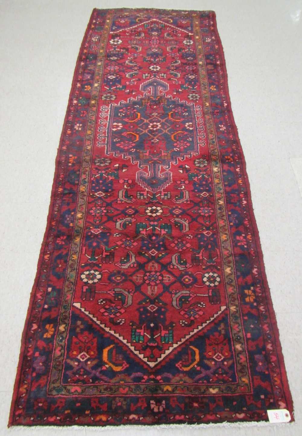 Appraisal: PERSIAN TRIBAL HALL RUG central geometric medallion and Herati floral