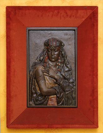 Appraisal: CONTINENTAL BRONZE-PATINATED AND POLYCHROMED METAL RELIEF OF A NUBIAN WOMAN