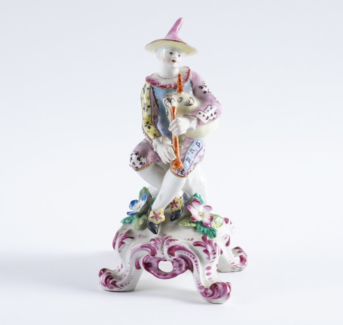 Appraisal: A BOW FIGURE OF HARLEQUIN Circa - Modelled seated playing