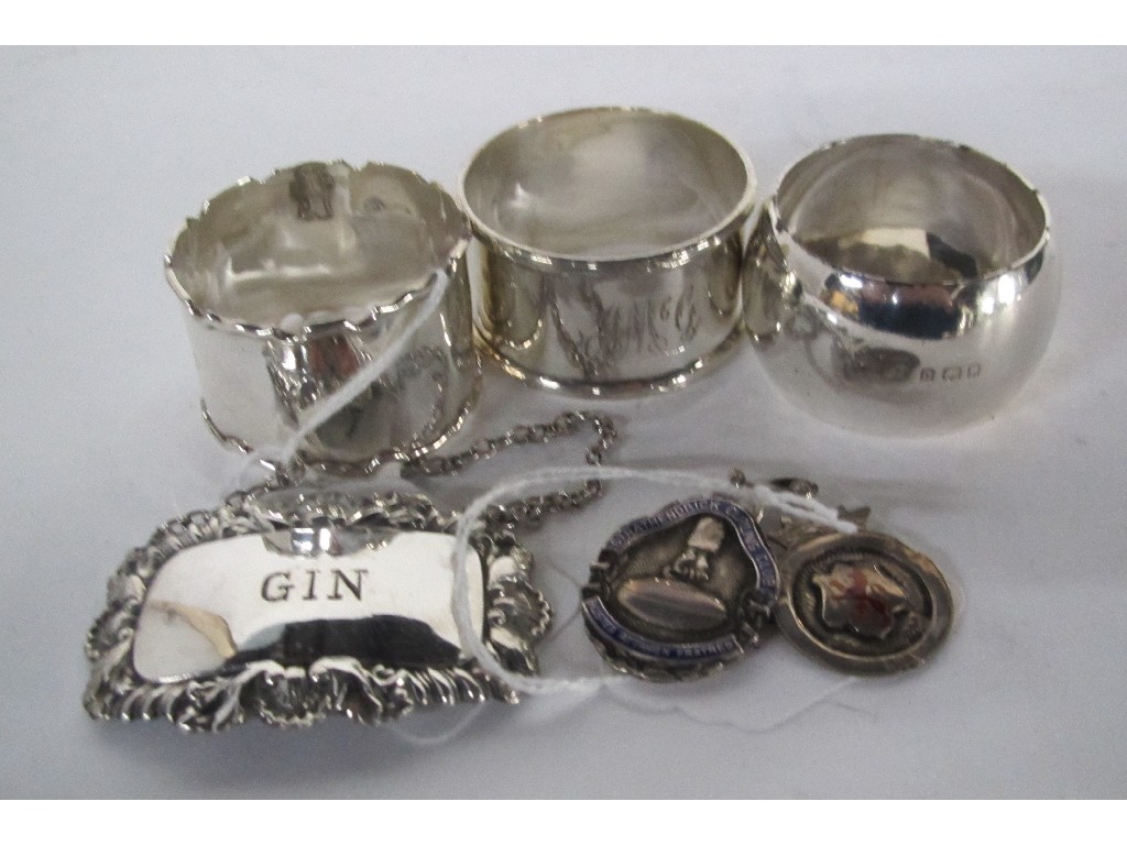 Appraisal: Lot comprising three silver napkin rings a decanter label and