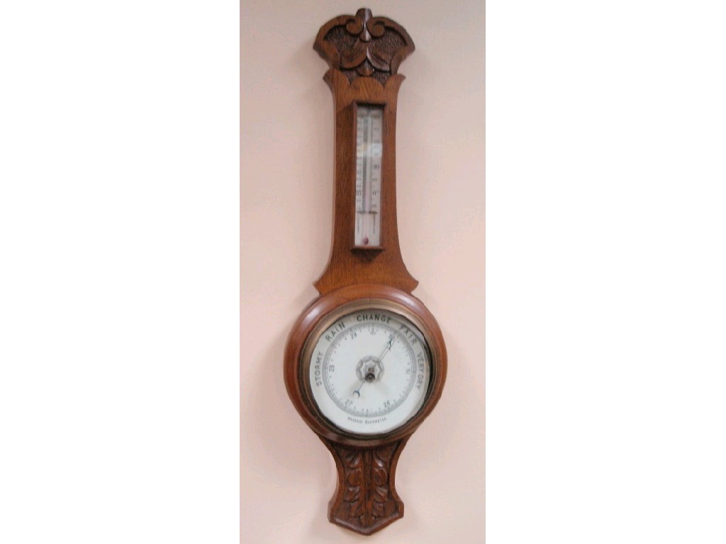 Appraisal: An Edwardian carved oak cased aneroid barometer with a thermometer