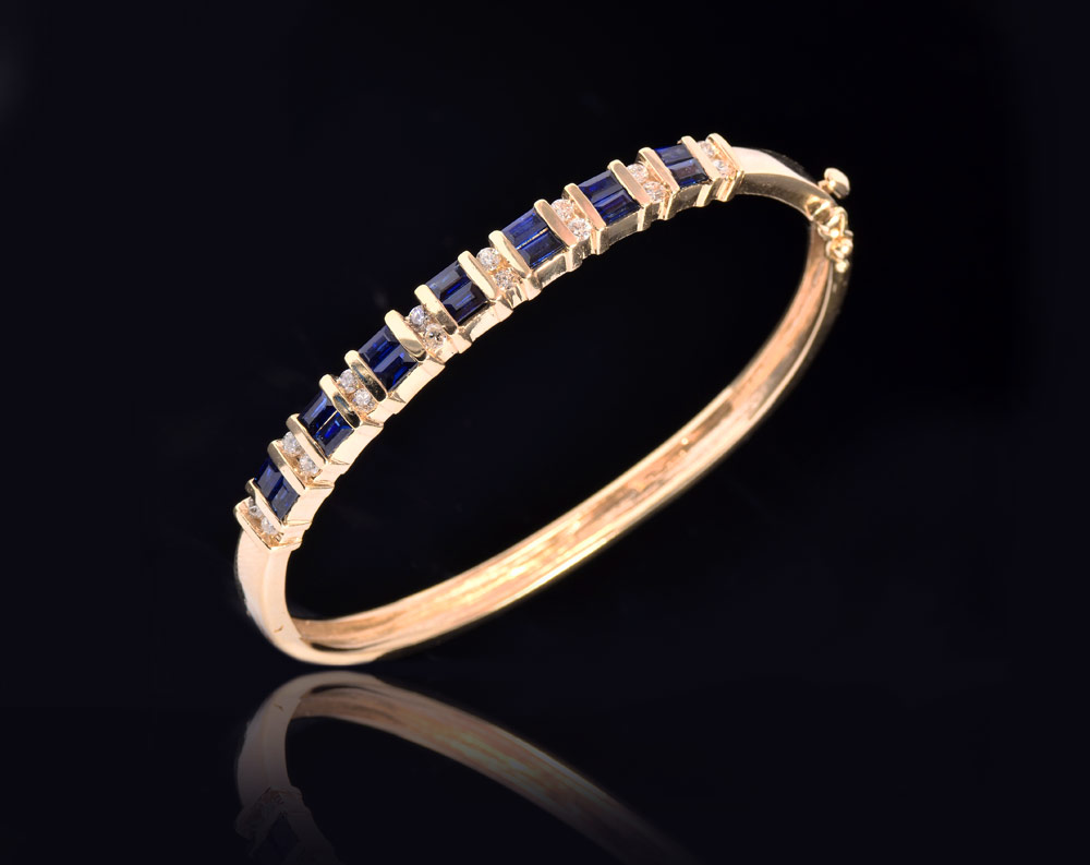 Appraisal: SAPPHIRE AND DIAMOND BANGLE BRACELET K yellow gold hinged bangle