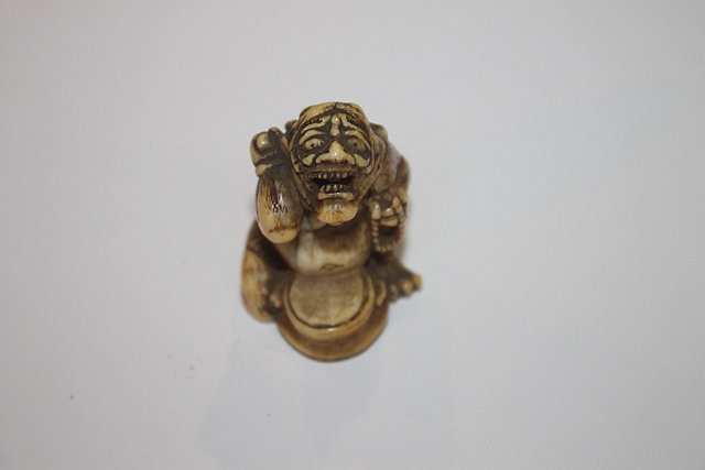 Appraisal: A JAPANESE IVORY NETSUKE of a seated oni beating a