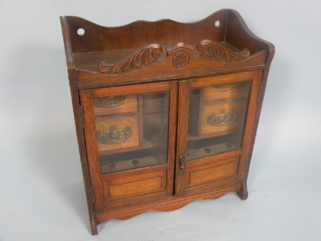 Appraisal: An Edwardian carved oak smokers cabinet with two glazed doors