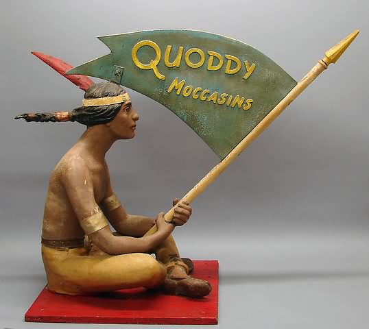 Appraisal: Indian brave seated cross-legged holding pennant --Quoddy Moccasins--on pole painted