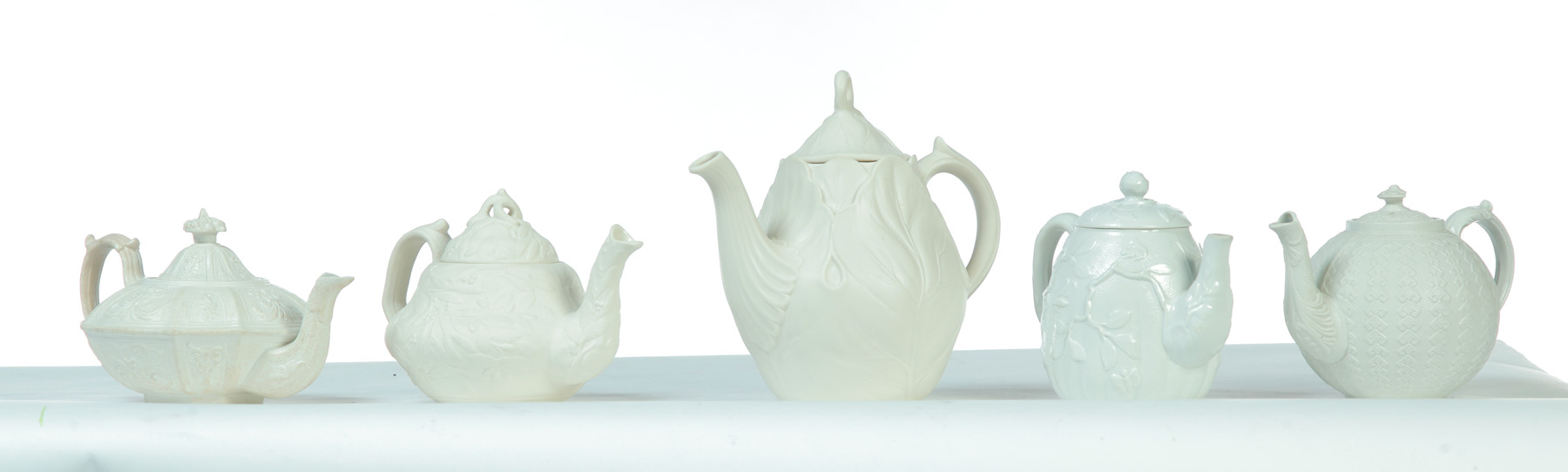 Appraisal: FIVE RELIEF MOLDED WHITE TEAPOTS England mid th century Various