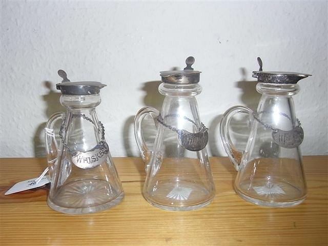 Appraisal: THREE GLASS WHISKEY TOTS with silver tops and labels