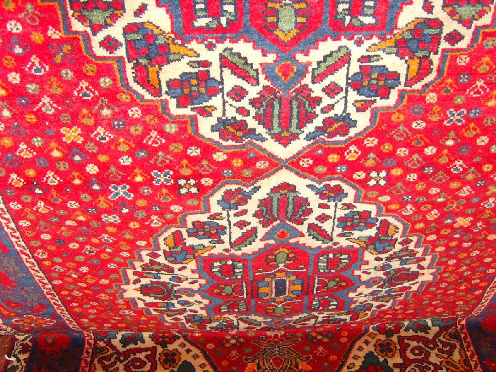 Appraisal: A red ground eastern wool rug with triple floral medallion