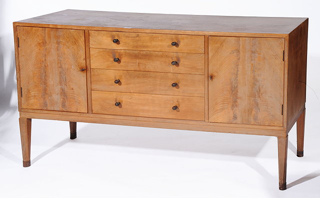 Appraisal: A COTSWOLD SCHOOL WALNUT SIDEBOARD with four graduated drawers to