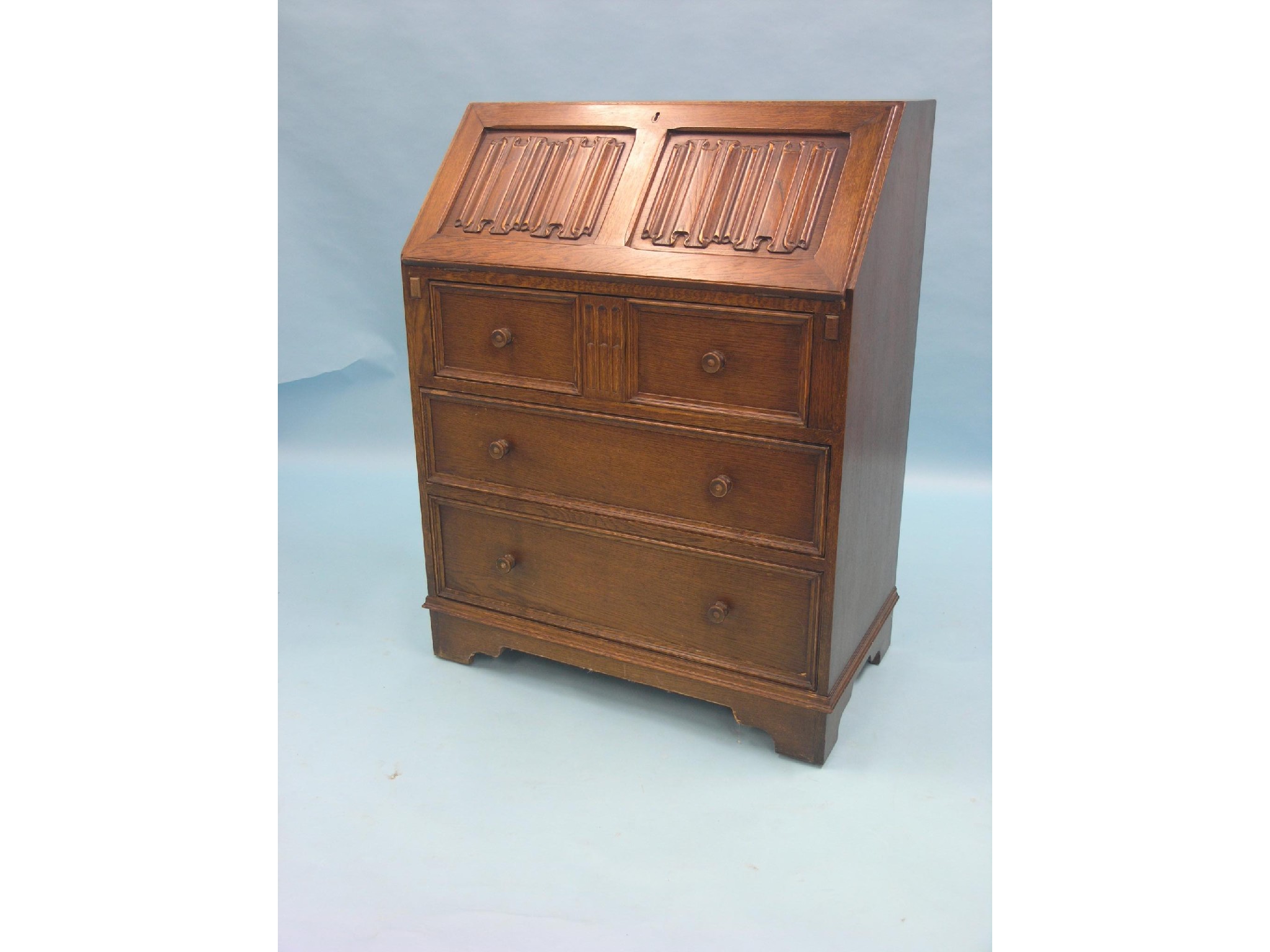 Appraisal: An oak linenfold bureau fall-front enclosing fittings three long drawers