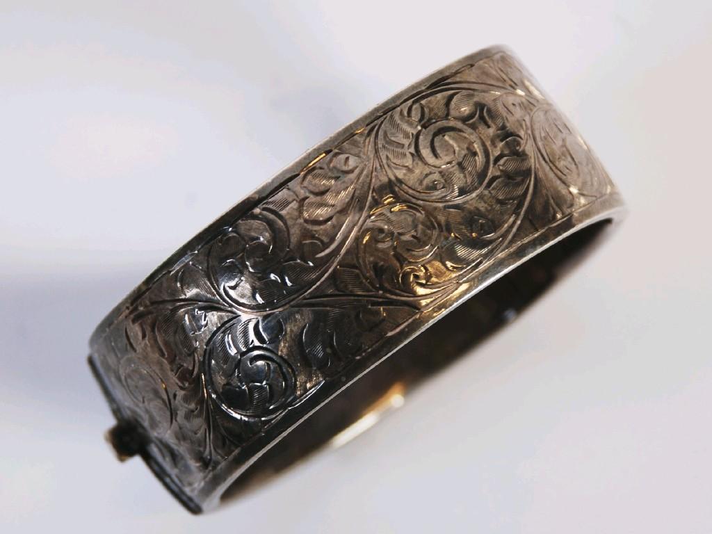 Appraisal: BROAD HINGE OPENING SILVER BANGLE the top foliate scroll engraved