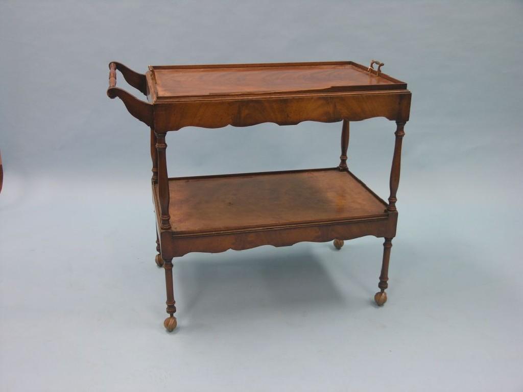 Appraisal: A mahogany-veneered two-tier trolley tray-top above shaped apron with single