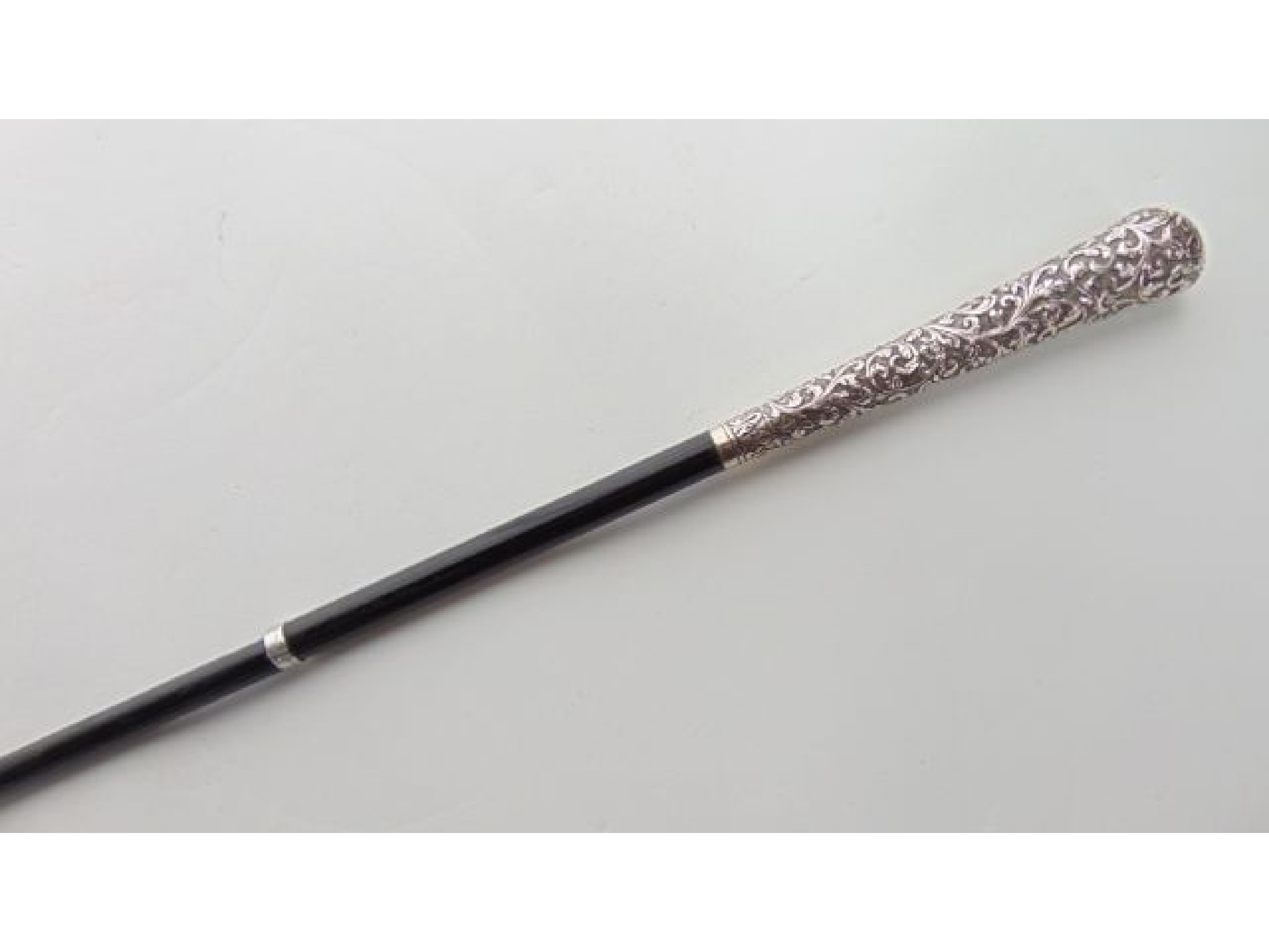 Appraisal: A slender ebonised walking cane terminating in an extensive embossed