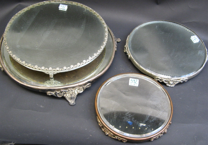 Appraisal: FOUR ROUND ORNATE MIRROR PLATEAUS footed metal bases beveled mirrors