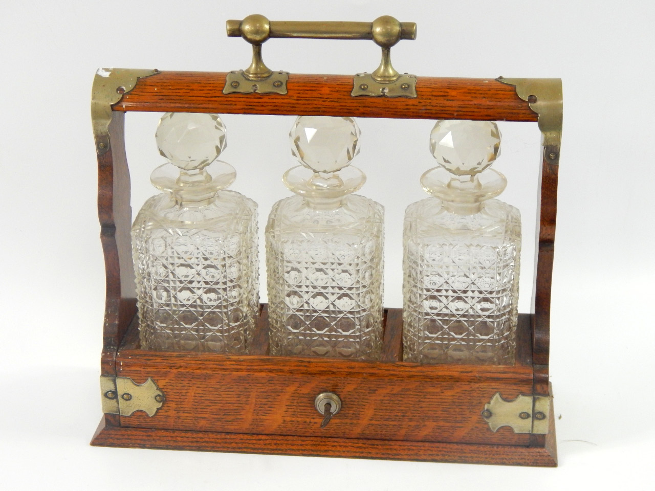 Appraisal: An oak and plated three bottle tantalus containing three hob