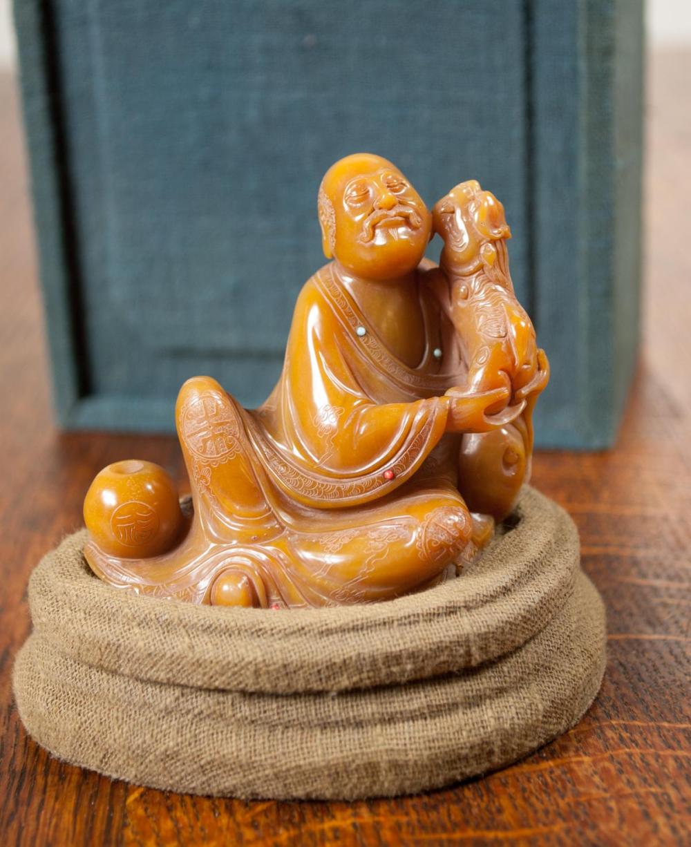 Appraisal: CHINESE CARVED SHOUSHAN SOAPSTONE LUOHAN SCULPTURE the seated figure holding