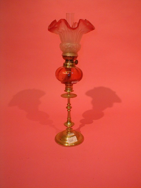 Appraisal: A turned brass oil lamp with cranberry reservoir and shade