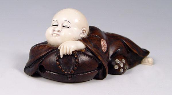 Appraisal: CARVED IVORY ROSEWOOD BUDDHA NETSUKE Resting Buddha with treasure bag