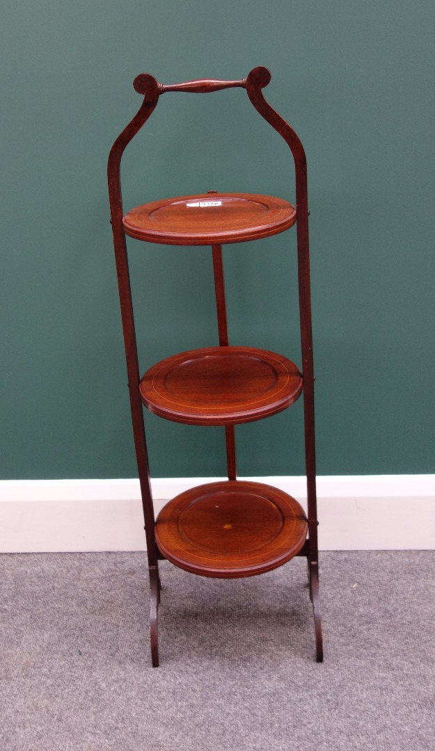 Appraisal: An Edwardian inlaid mahogany circular folding three tier cake stand