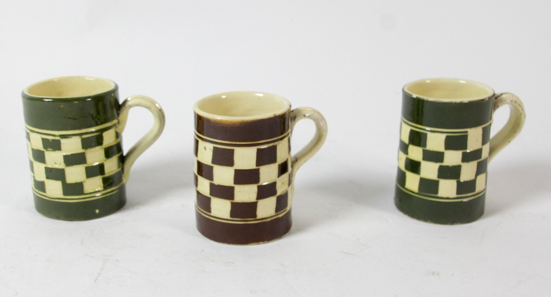 Appraisal: Two green glazed slipware mugs with chequered decoration and another