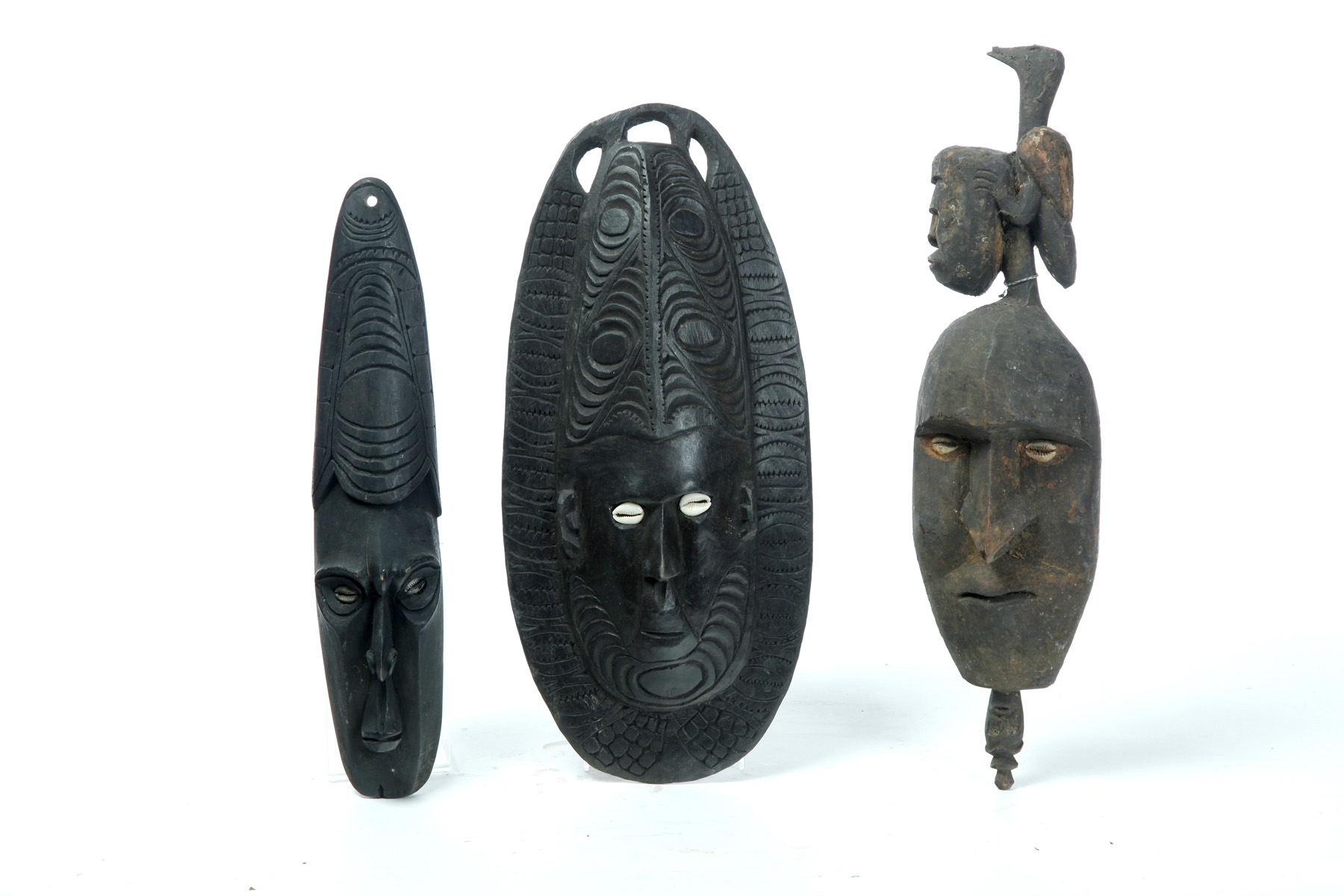 Appraisal: THREE PAPUA NEW GUINEA CARVED MASKS Twentieth century Cowrie shell